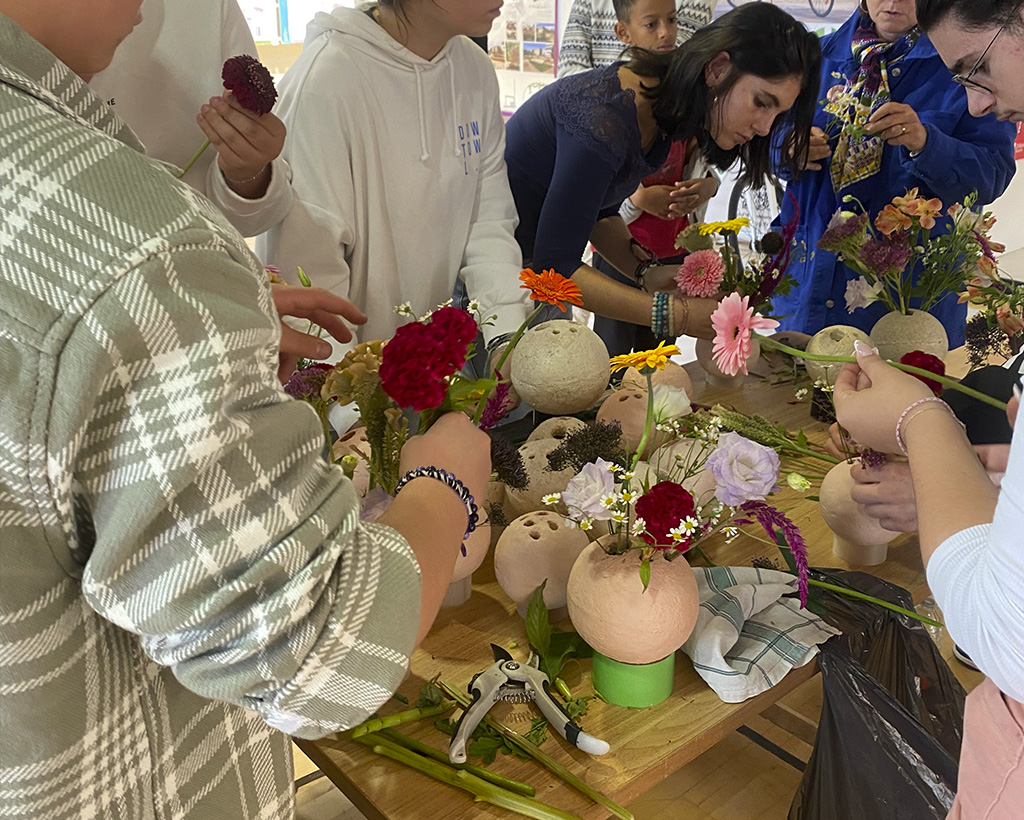 Atelier floral in situ avant le vernissage : création d'un centre de table pour fleurir l'exposition avec les vases en mycélium Boutures et en réemployant les restes de la scénographie (verreries, scotchs colorés etc...).